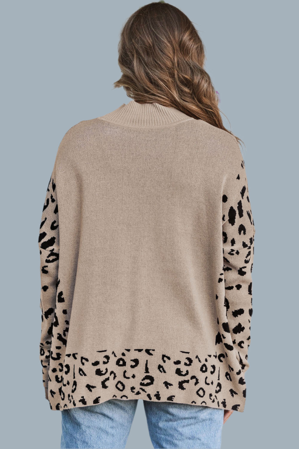 Person wearing a beige sweater with leopard print sleeves against a white wall.