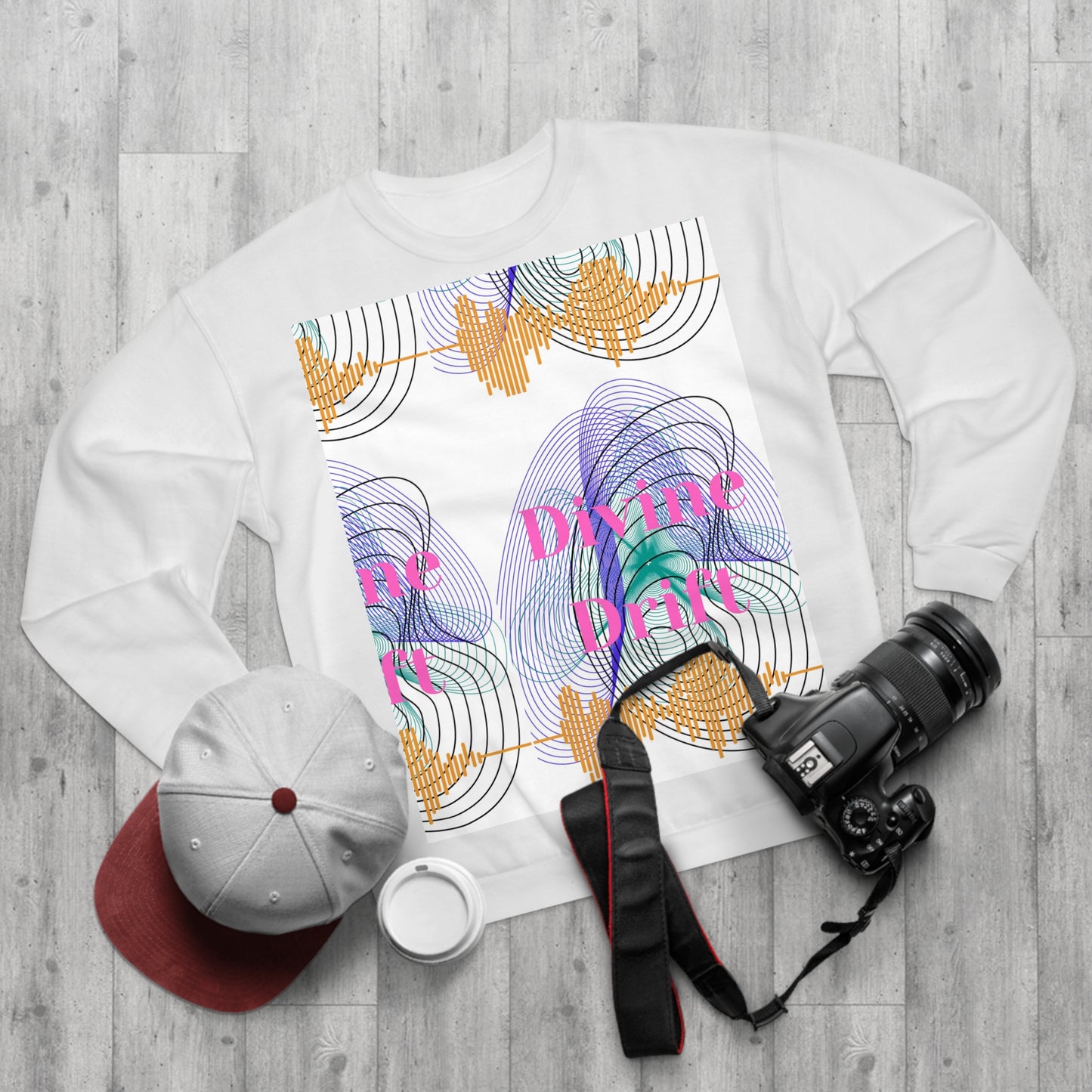White sweatshirt with colorful design and text on a wooden surface with a camera and cap.