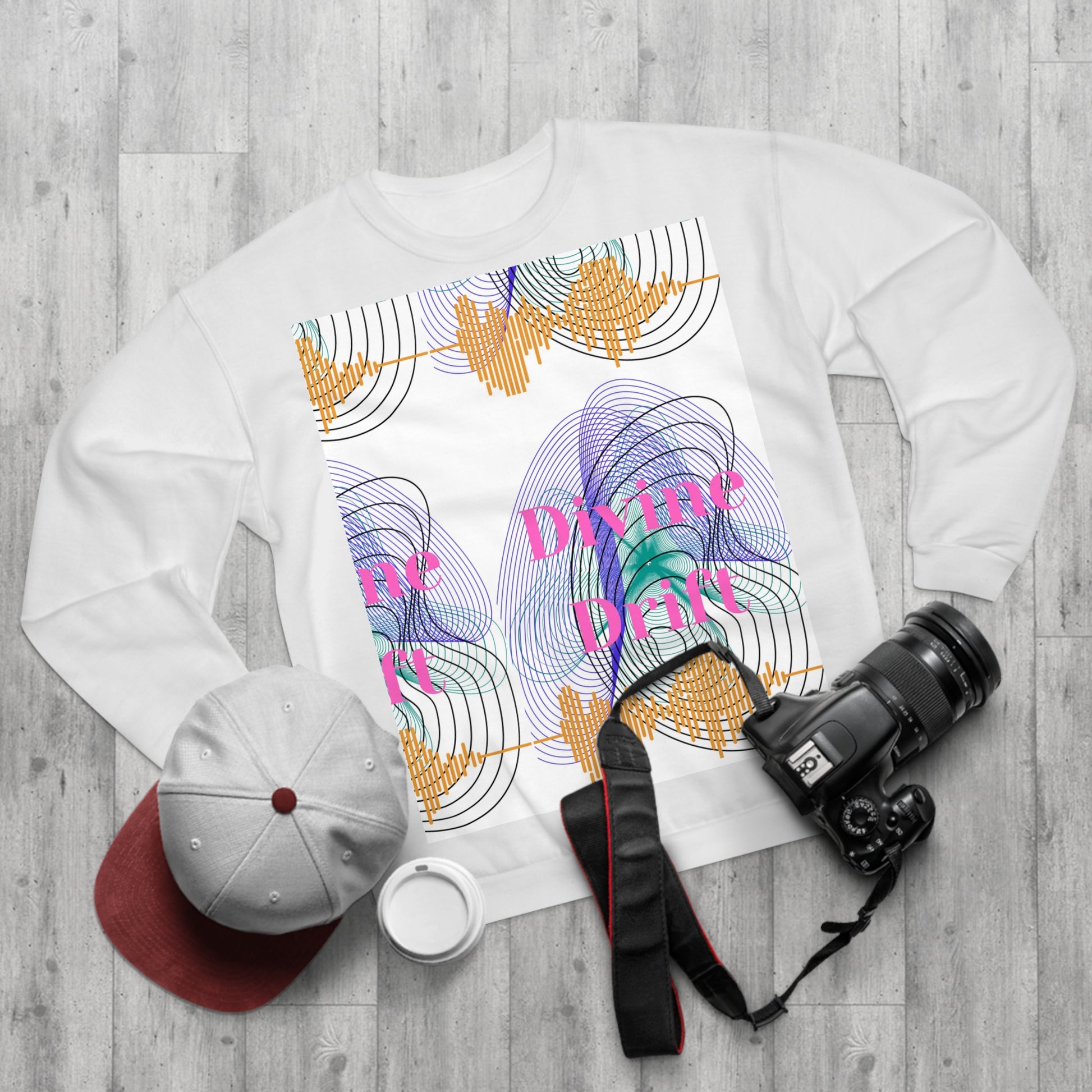 White sweatshirt with colorful design and text on a wooden surface with a camera and cap.