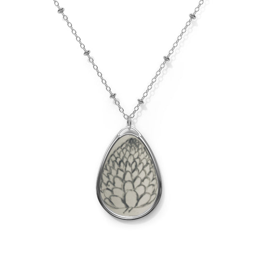 Teardrop-shaped pendant with floral design on a silver chain against a white background