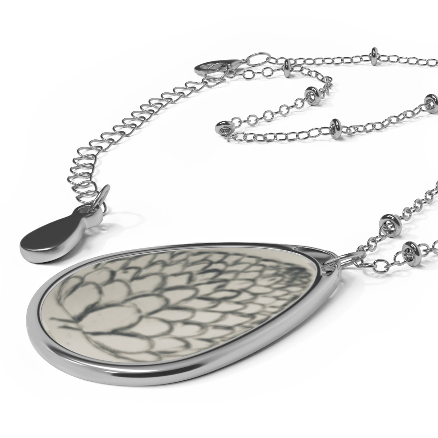 Teardrop-shaped pendant with a detailed pattern on a silver chain against a white background